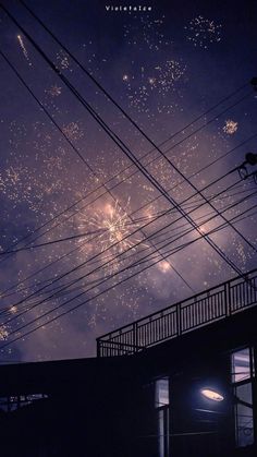 fireworks are lit up in the night sky above power lines and telephone poles, as seen from an alleyway