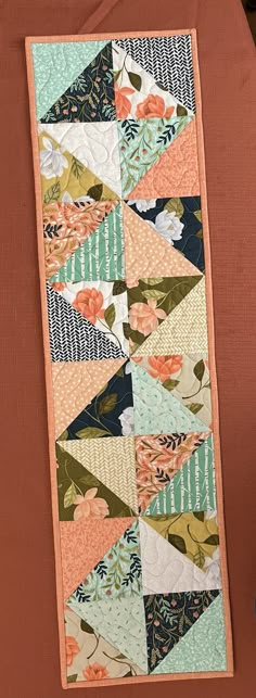 a quilted table runner with an orange and blue flower design on it's side