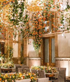 an indoor dining area with tables, chairs and flowers hanging from the ceiling over them