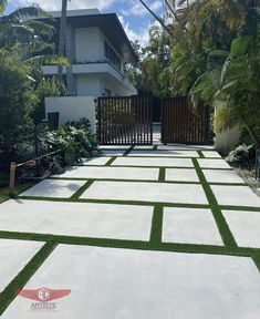 an outdoor walkway with artificial grass in front of a white house and palm trees on the other side