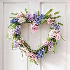 a heart shaped wreath with purple and pink flowers on it hanging from a white door