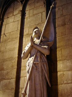 a statue of a woman holding a staff in front of a brick wall