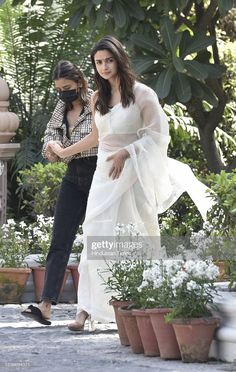 the actress is seen walking with her friend in front of some potted plants and flowers