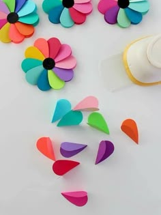 colorful paper flowers next to a cup with a sippy bottle on the side and several petals scattered around it