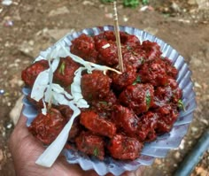 a hand holding a bowl filled with meatballs and coleslaw next to a stick