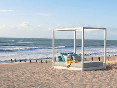 a white bed sitting on top of a sandy beach next to the ocean with blue skies