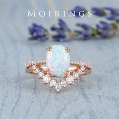 a white opal and diamond ring sitting on top of a table next to lavender flowers