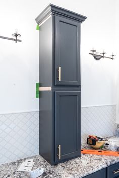 a tall gray cabinet sitting on top of a kitchen counter next to a wall mounted towel dispenser