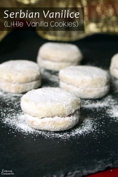 several powdered sugar cookies are on a black plate with gold sebran vanilla