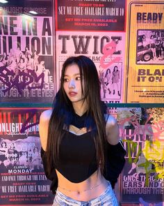 a woman standing in front of a wall with posters on it's walls behind her