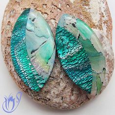 two green leaf shaped earrings sitting on top of a rock