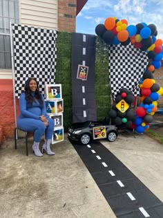 a woman sitting on a chair in front of a balloon arch with cars and balloons