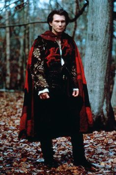 a man standing in the woods wearing a red and black cloak with dragon designs on it