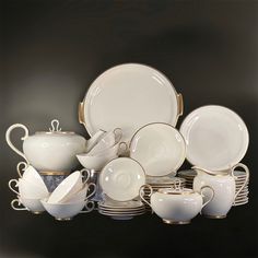 a collection of white dishes and cups with gold trimmings on the rim,