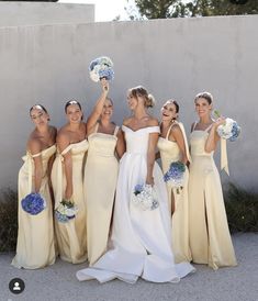 a group of bridesmaids pose for a photo in front of a wall with their bouquets