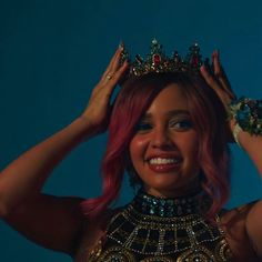 a woman with pink hair wearing a tiara and smiling at the camera while standing in front of a blue background