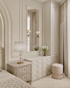 an elegant bedroom with white furniture and flowers in vases on the dresser next to the bed