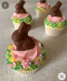 four cupcakes decorated with chocolate bunny ears and pink frosting, on a table