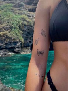 a woman's arm with three butterflies on it and the water in the background