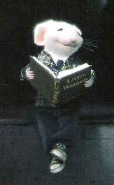 a white mouse reading a book while sitting on the ground in front of a black background