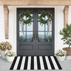 a black and white striped door mat with two wreaths on it, next to potted plants