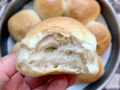 a hand holding a piece of bread in front of some buns on a plate