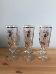 three wine glasses sitting on top of a wooden table next to each other with gold designs