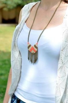 a woman wearing a white tank top and blue jeans with a necklace on her neck