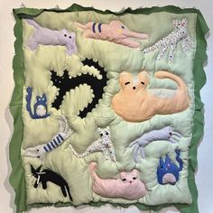 a quilted wall hanging with cats and dogs on it's sides, all in pastel colors