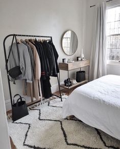 a bedroom with a bed, mirror and clothes rack in the corner next to a window