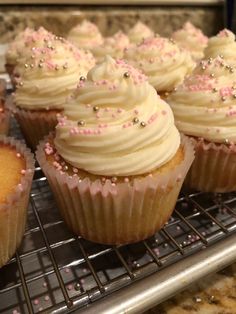 cupcakes with white frosting and pink sprinkles on a cooling rack