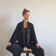 a woman sitting on top of a wooden stool wearing black pants and a cardigan