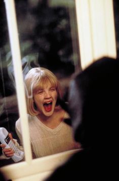 a woman laughing and holding a remote in front of a mirror with her mouth open