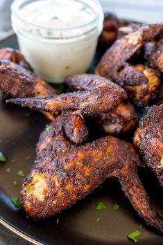 some chicken wings on a black plate with ranch dressing in the background and a small bowl of ranch dressing