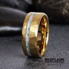 a gold ring with green and white stones on it's side, sitting on a table