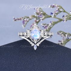 a white ring with an opal center surrounded by diamonds and other jewelries sits on top of a blue surface