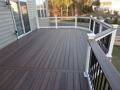 a wooden deck with white railings next to a home's front door and windows