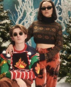 two people standing next to each other in front of a christmas tree