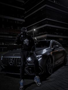 a man sitting on the hood of a car in front of a building at night