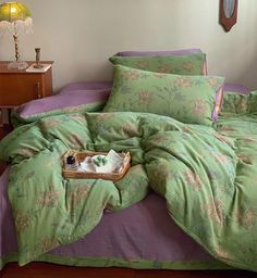 an unmade bed with green and purple comforter on it, next to a night stand