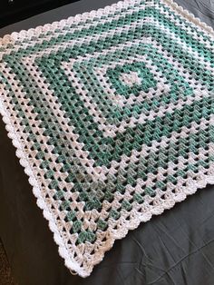 a green and white crocheted blanket sitting on top of a bed next to a pillow