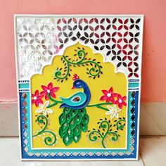 an intricately designed card with a peacock sitting on a tree branch in front of a pink wall