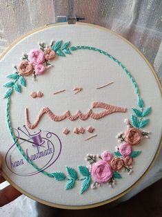 someone is holding up a embroidery project that has been made with pink and green flowers