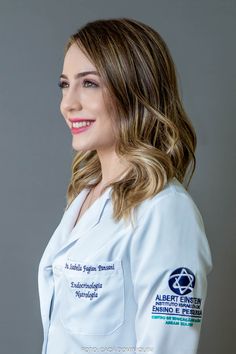 a smiling woman wearing a white lab coat with blue writing on the front and back