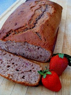 a loaf of banana bread and two strawberries on a cutting board