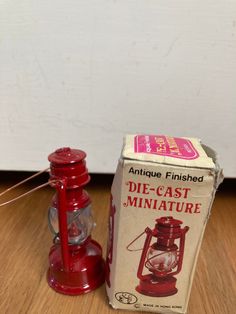 an old fashioned red miniature lamp next to a box