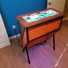 an orange and brown table with two drawers on it in front of a blue wall