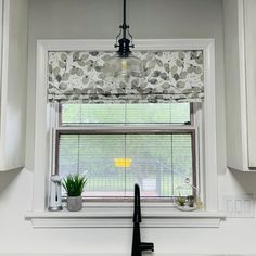 a kitchen window with blinds and plants on the windowsill, in front of white cabinets