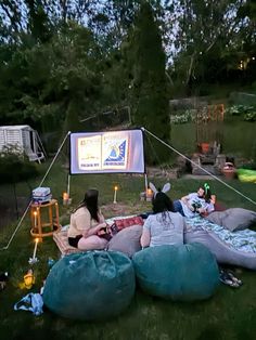 two people sitting on bean bags in the grass watching a movie at an outdoor event