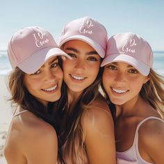 three beautiful young women wearing pink hats on the beach